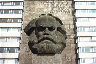 A huge bust of a bearded man sits in front of a multi-floored building.