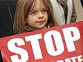 A young girl holds up a red sign with white letters that reads "Stop".
