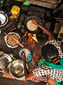 An overhead photograph taken of a woman in India cooking over an open flame, while her infant sleeps nearby on a cut open burlap sack. 