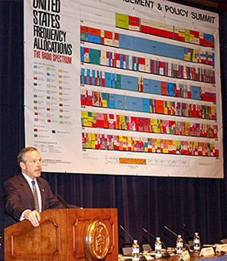 Commerce Secretary Evans presenting in front of a chart of the electromagnetic spectrum.