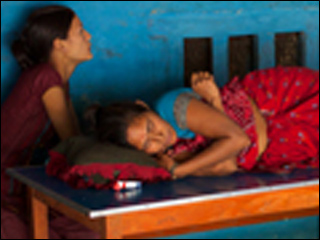 Tiwali sits across from a woman watching TV and another napping at a small colorful tea shop.