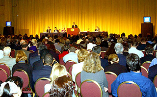 Photograph of speaker presenting to a large audience.
