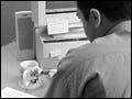 Black-and-white photograph of a businessman writing a memo in front of a computer.
