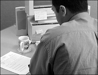 Black-and-white photograph of a businessman writing a memo in front of a computer.