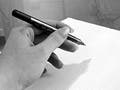 Black and white photo of a hand holding a pen, prepared to write on a sheet of paper.