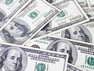 Close-up of a pile of one-hundred dollar bills that are spread out on a surface.