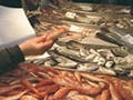 A fishmonger and a customer interacting across a counter covered with bins of fish in Venice's Rialto Markets.