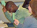 Students sitting in class raise their hands while holding green notecards.