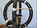 A photo of an electromagnetic device. It looks like a spokeless unicycle with another ring crossecting it and wires connected to it.