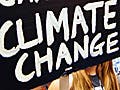In the midst of a crowd, a young woman holds a sign with the words: System Change. Not Climate Change.