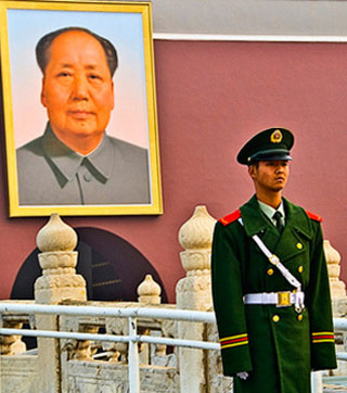 A guard in Beijing stands in front of the imperial palace where a large photo of Mao Zedong hangs.