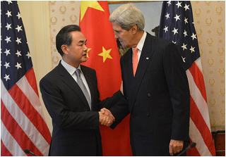 Two suited men shake hands in front of American and Chinese flags.