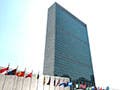 A tall glass and concrete structure fronted by the colorful flags of various nations.