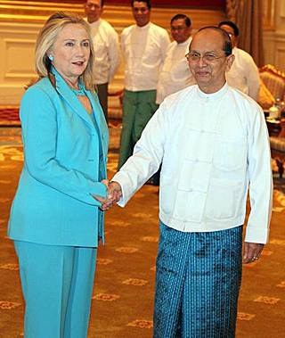 Hillary Clinton, in a teal pants suit, shakes the hand of Thein Sein, who is wearing a white buttoned shirt and teal lungi, a traditional Burmese garment, like a sarong.
