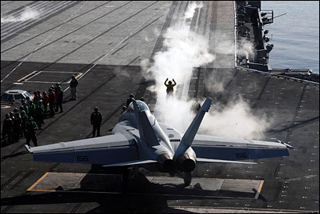 Image depicts an aircraft and navy personnel on the deck of an aircraft carrier.
