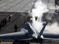 Image depicts an aircraft and navy personnel on the deck of an aircraft carrier.