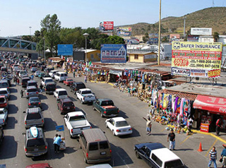 Cars wait in line on a road lined with shops at the US/Mexican border.