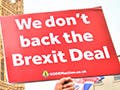 In the midst of a crowd, a man carries signs with the words: “The Brexit Mess!” and “We Don’t Back the Brexit Deal.” 