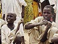 Children from the Sudan crouch on the ground playing with clay figures.