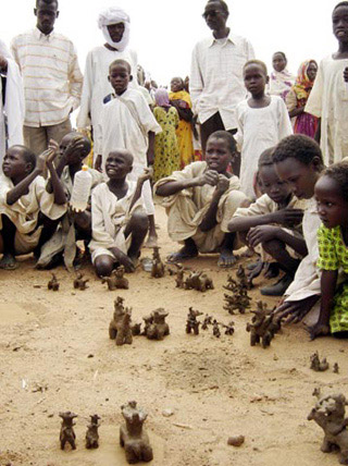 Children from the Sudan crouch on the ground playing with clay figures.