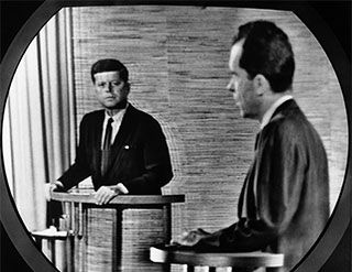The grainy image on a television screen shows John F. Kennedy and Richard Nixon standing at podiums.