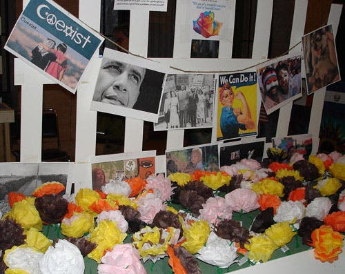 Multi-colored paper roses lie in front of photos of people of different ethnicities.