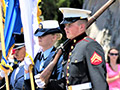 A group of six men and two women, all-uniformed, with some carrying colorful flags, marches in formation.