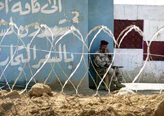 A photo of an Iraqi Army soldier seated behind a barbed wire fence.