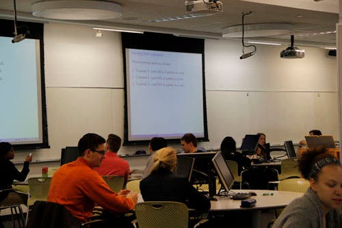 A multiple choice question is shown on a projector screen. Students use handheld clickers to submit their answers.