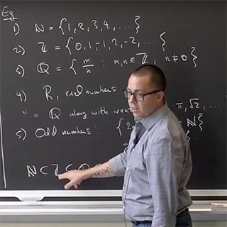 A man standing in front of a blackboard and pointing to some text on the blackboard.