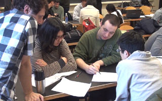 Four people working over papers laid out on a desk.