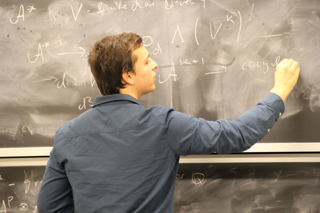 A male student writing on a blackboard with chalk.