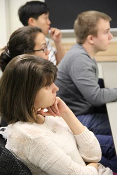 Two women and two men sitting in chairs at a table; they look toward a speaker at the front of the room.