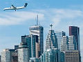 Photograph of the Toronto skyline seen from over the water, with a commercial jet in flight over the skyline and boats visible near the harbor.