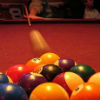 Photo of a billiards player midway through shooting the cue ball toward the rest of balls, still in rack formation.