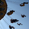 Photograph of people on a ride with a round central structure with swings hanging down from it and with the central structure spinning quickly enough for the people on the swings to feel a force away from the center of the ride.