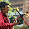 A man in a red collared shirt and an old-fashioned hat juggles flaming torches.
