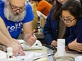 Four students and one professor leaning over a table pointing and looking at items and papers on the table.