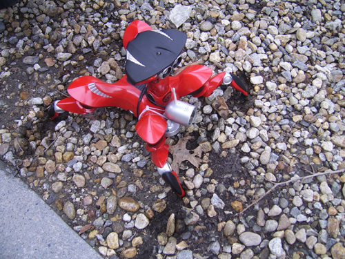 Close-up of the red crawler robot with a sensor attached to the front, moving across pebbles.