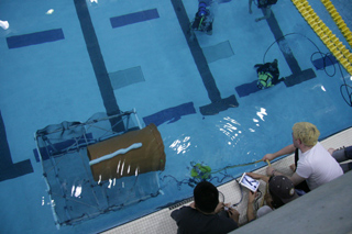 Students attempt to maneuver their robot into a garbage can anchored on its side on the bottom of the pool.