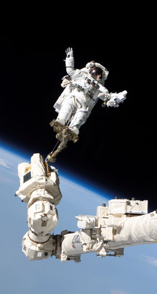 Astronaut Steve Robinson in space, standing on a long robotic arm.