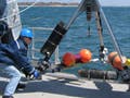 Three people winching large tripod off deck into ocean.