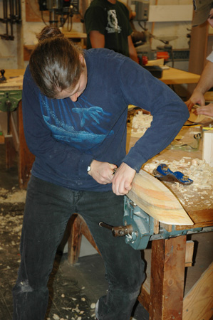 A student refines her hull model's shape with a plane.