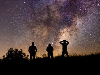 Three silhouetted figures look at a star-filled sky.