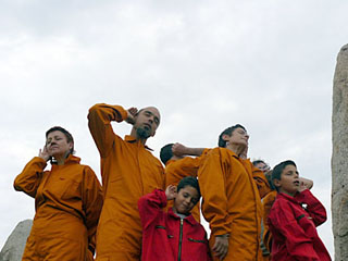 Photo of a small group of adults and children, wearing colored jumpsuits and in various poses of concentrated listening.