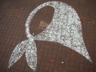 An image of a white shawl tied at the neck is superimposed on a red brick background.