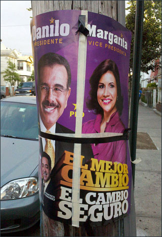 A colorful poster with a smiling man and woman is attached to a telephone pole.