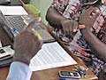 A translator and interview subject sign to one another as an anthropologist watches.