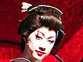 A small, keen-featured man, clothed in a kimono, and wearing powder on his face and rouge on his lips, sits in a carriage.