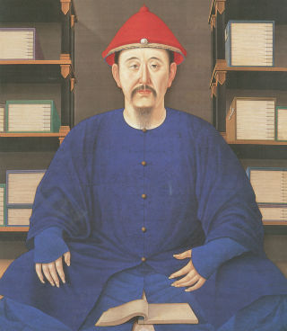 Gentleman wearing robes sits cross-legged on the floor reading a book.